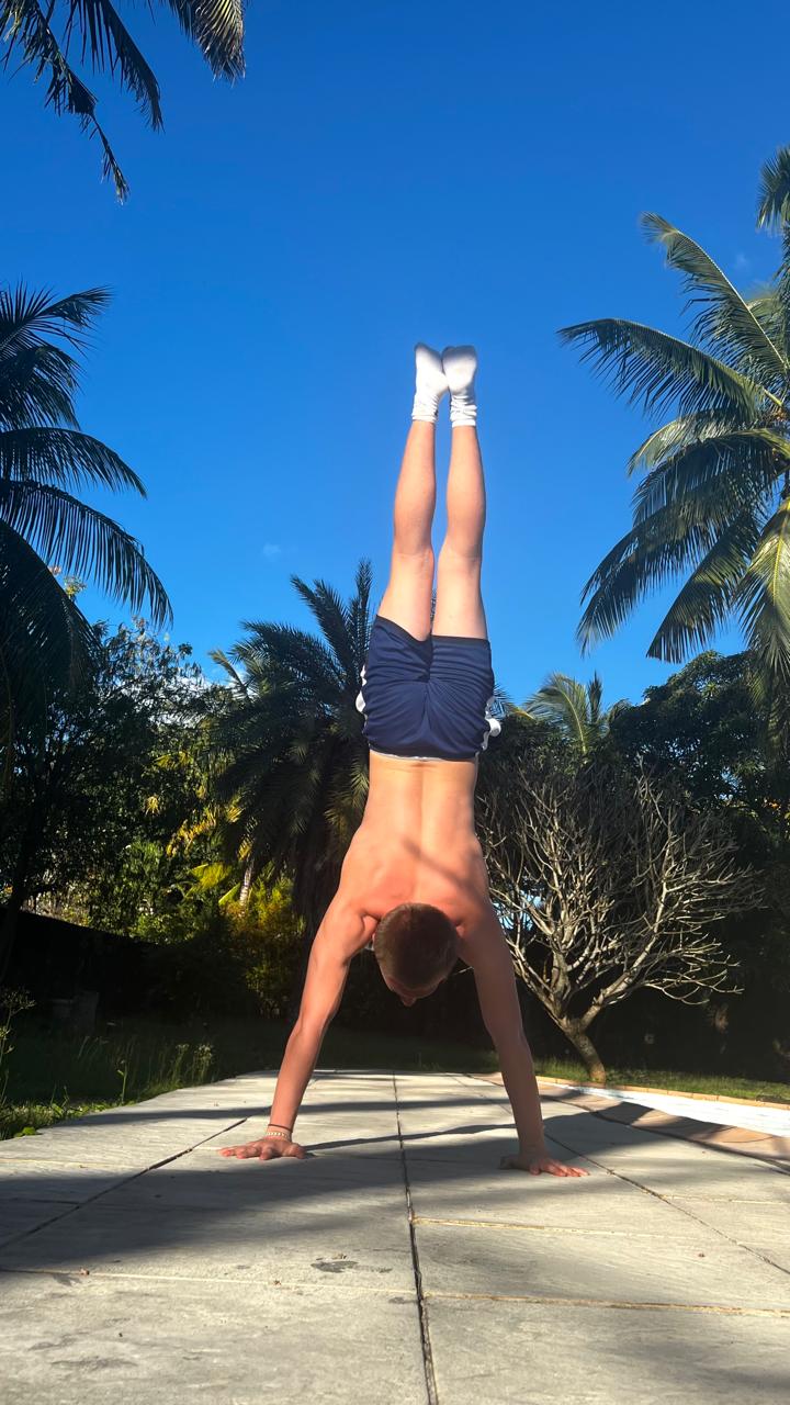 Sacha en handstand sur une terrasse au soleil, entouré de cocotiers